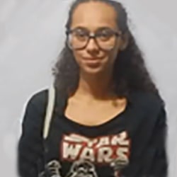 Mulher negra com cabelo encaracolado com óculos de grau e camiseta preta e escrita Star Wars em Vermelho.