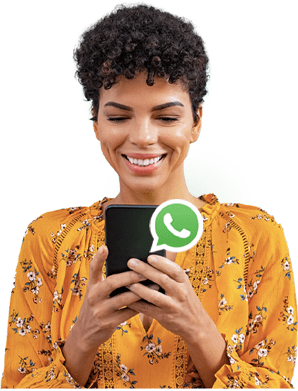 Mulher negra com cabelos encaracolados, segurando e olhando para o celular que está em suas mãos e um ícone do WhatsApp sobre o celular.