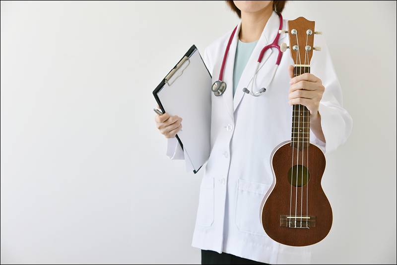 Mulher com jaleco branco e estetoscopio segurando uma prancheta e um ukelele.